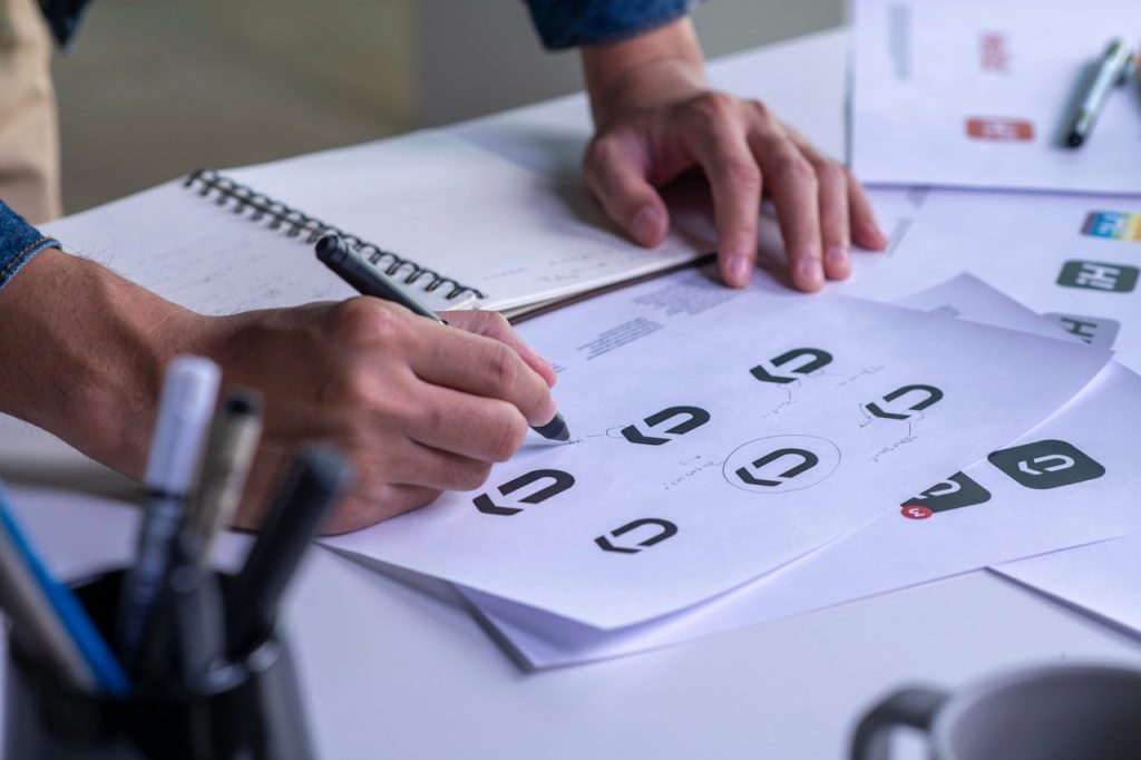 Hände zeichnen Symbole auf Papier am Schreibtisch